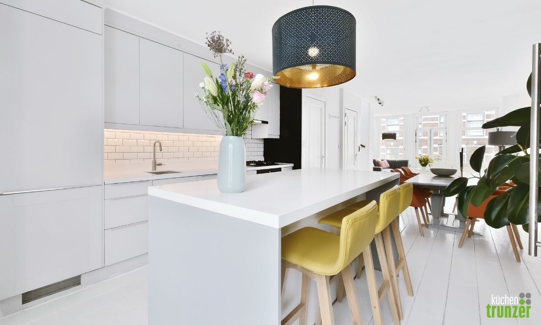 Moderne Küche mit einem langen weißen Tisch, gelben Stühlen und einem Blumenstrauß in einer Vase.