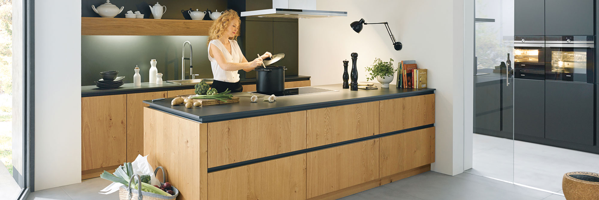Frau, die in einer modernen Küche mit Holz- und schwarzen Elementen kocht.