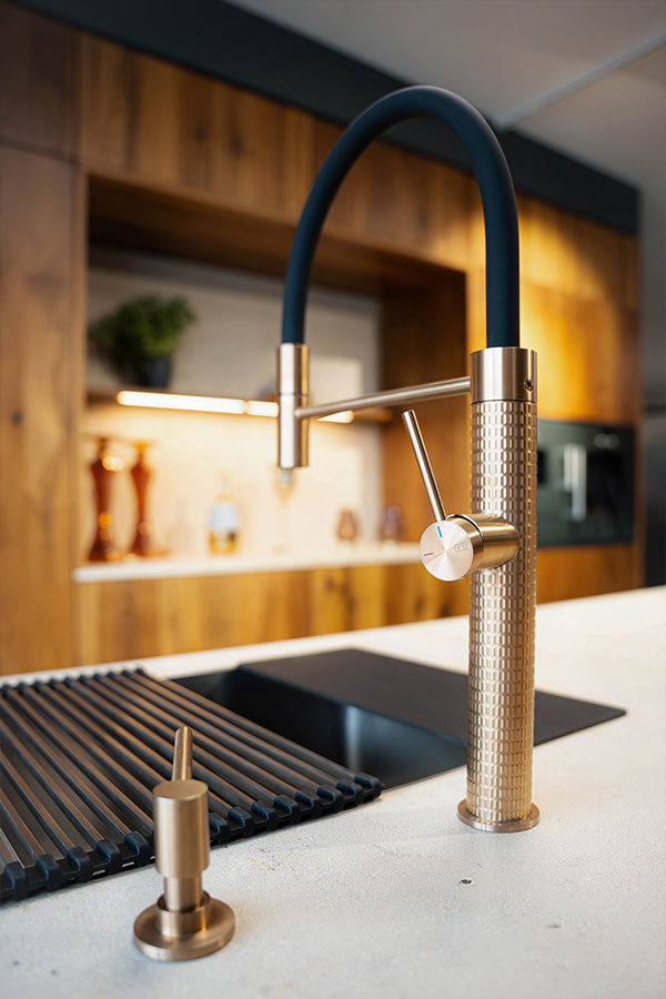 Moderne Küchenarmatur mit einem goldenen Körper und schwarzem Schlauch auf einer Arbeitsplatte.
